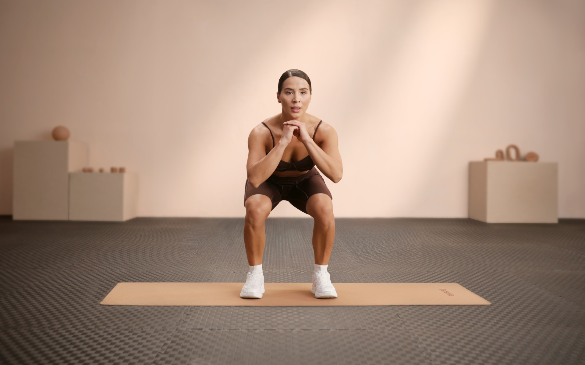 Woman performing bodyweight squats on an exercise mat as part of a cardio 7 days a week routine.