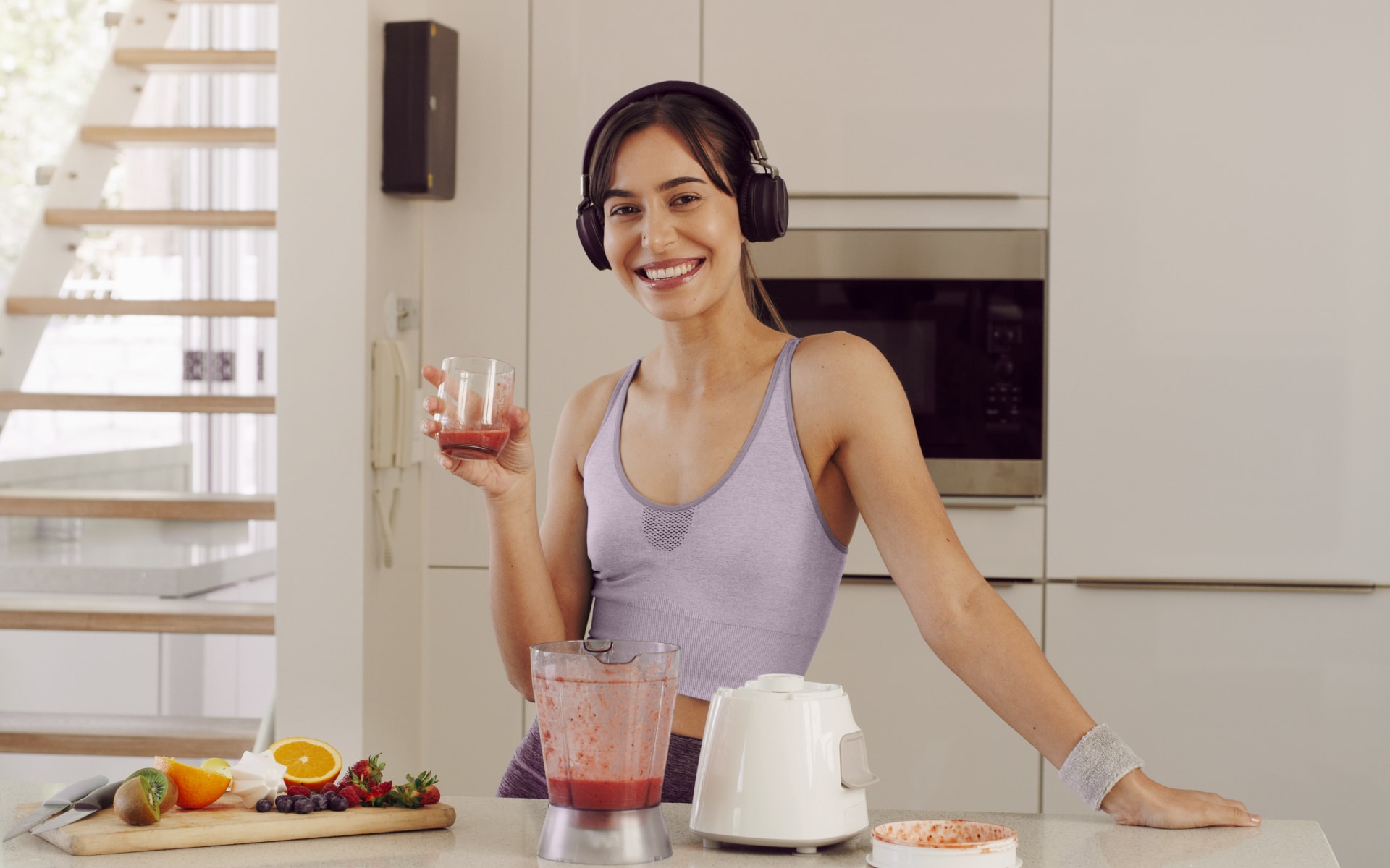 Woman holding a berry smoothie in a bright kitchen, illustrating a 72 hour fast and the transition back to nourishment after an extended fasting period.