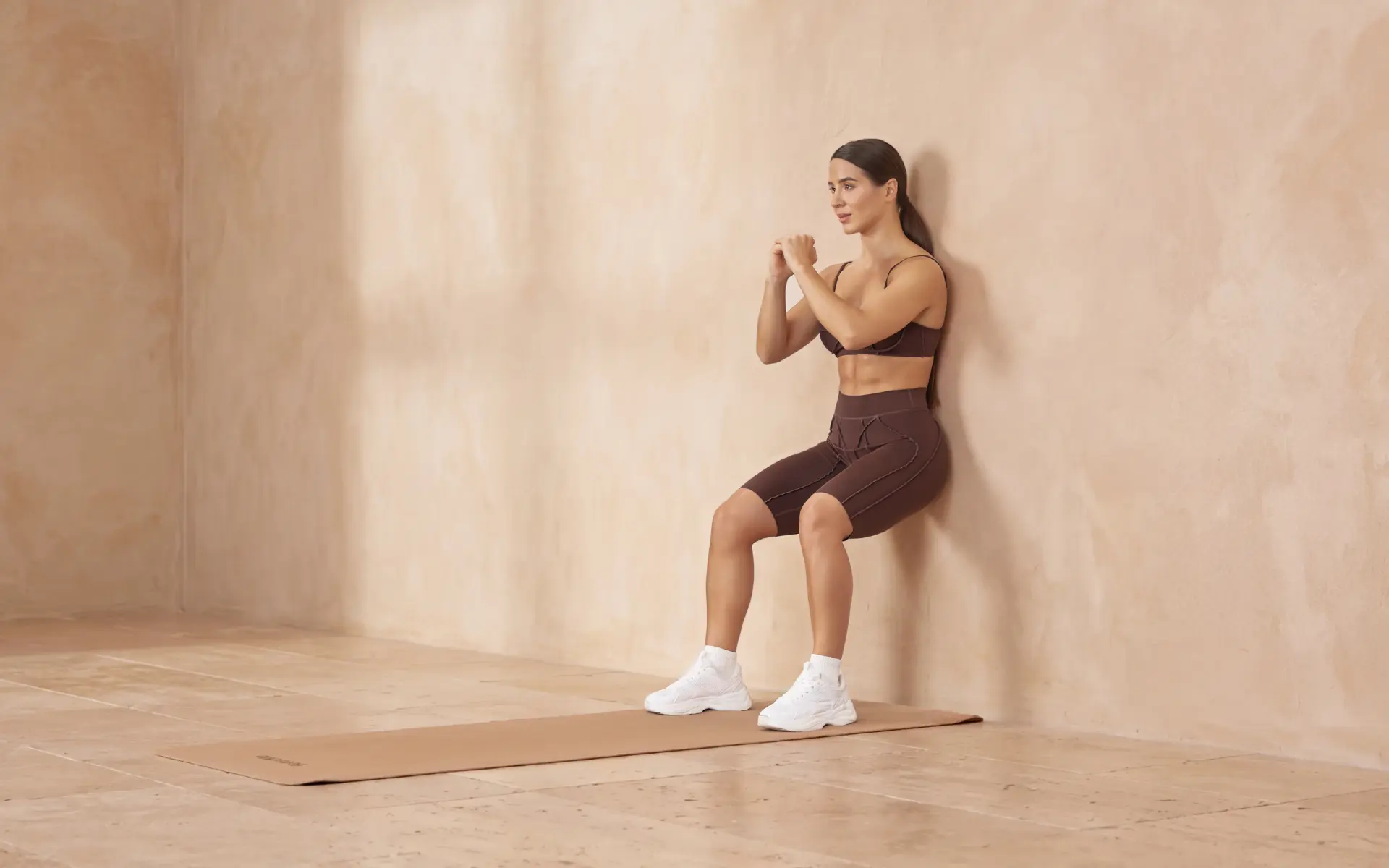 Woman performing a wall sit on a mat to demonstrate wall sitting benefits.