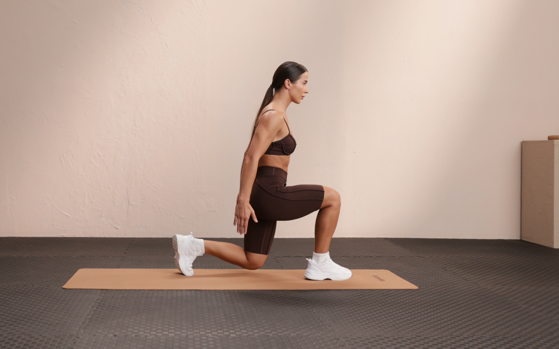 Woman performing a forward lunge on an exercise mat during a 2-day split workout.