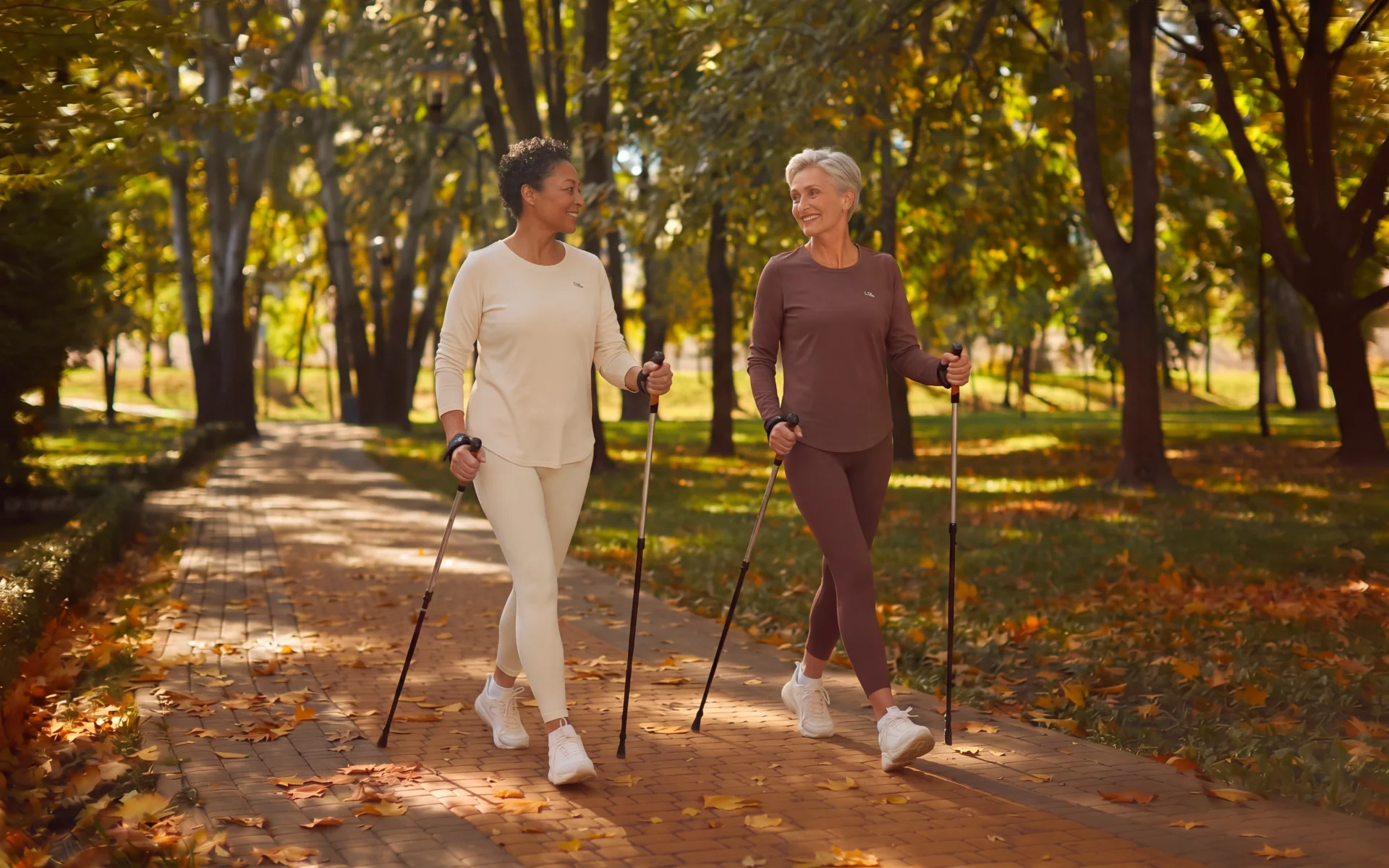Two older women Nordic walking with poles in a park for Nordic walking disadvantages.