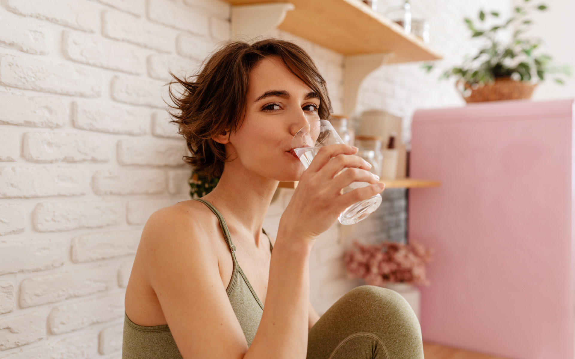 Woman drinking a glass of water in a cozy kitchen, illustrating fasting drinks and simple hydration choices during a fast.