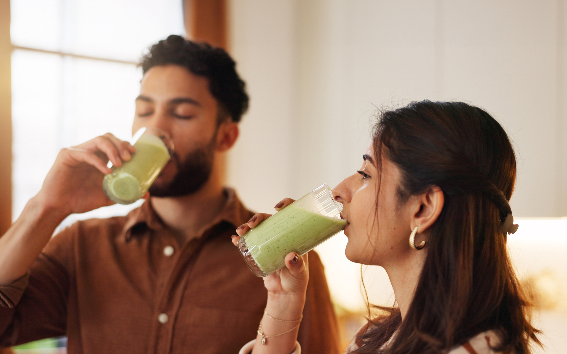 Man and woman drinking green smoothies at home, illustrating fasting detox and nutrient-rich drinks as part of a wellness routine.
