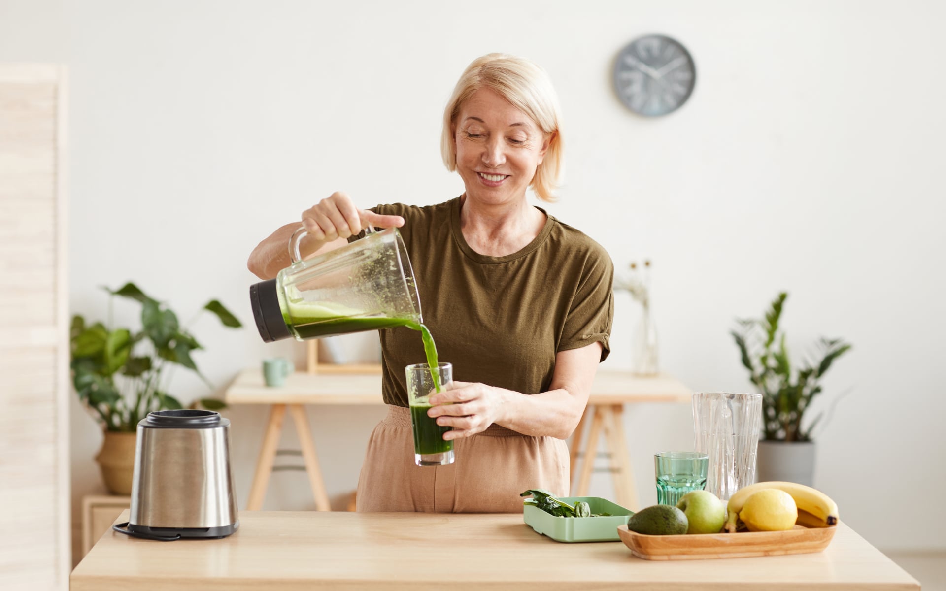 Woman over 50 pouring a green smoothie in a bright kitchen, illustrating intermittent fasting for women over 50 and balanced nutrition during eating windows.