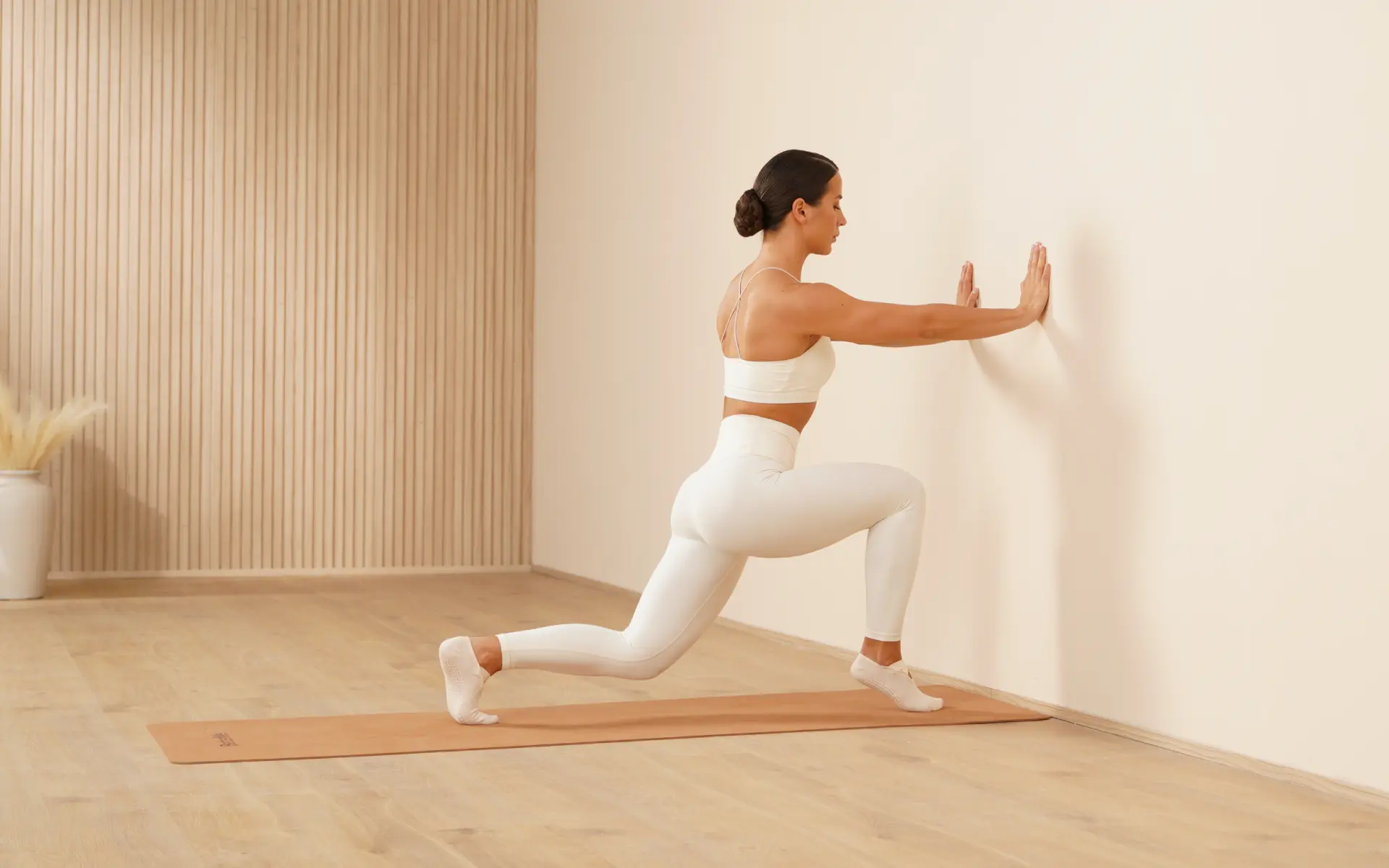 Woman performing a Pilates lunge with wall support for does Pilates help lose belly fat.