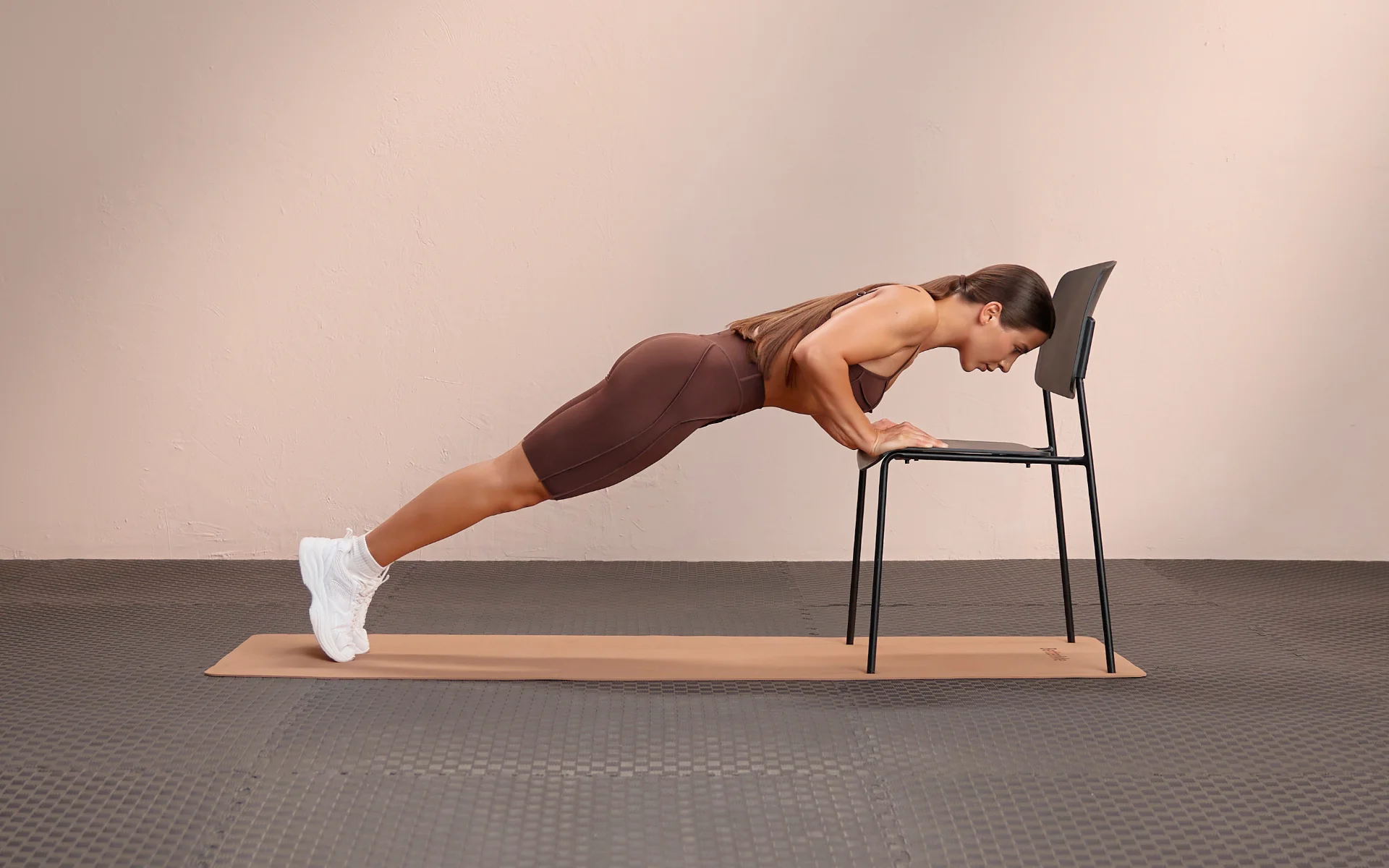 Woman performing an incline push-up on a chair for bodyweight exercises for chest.