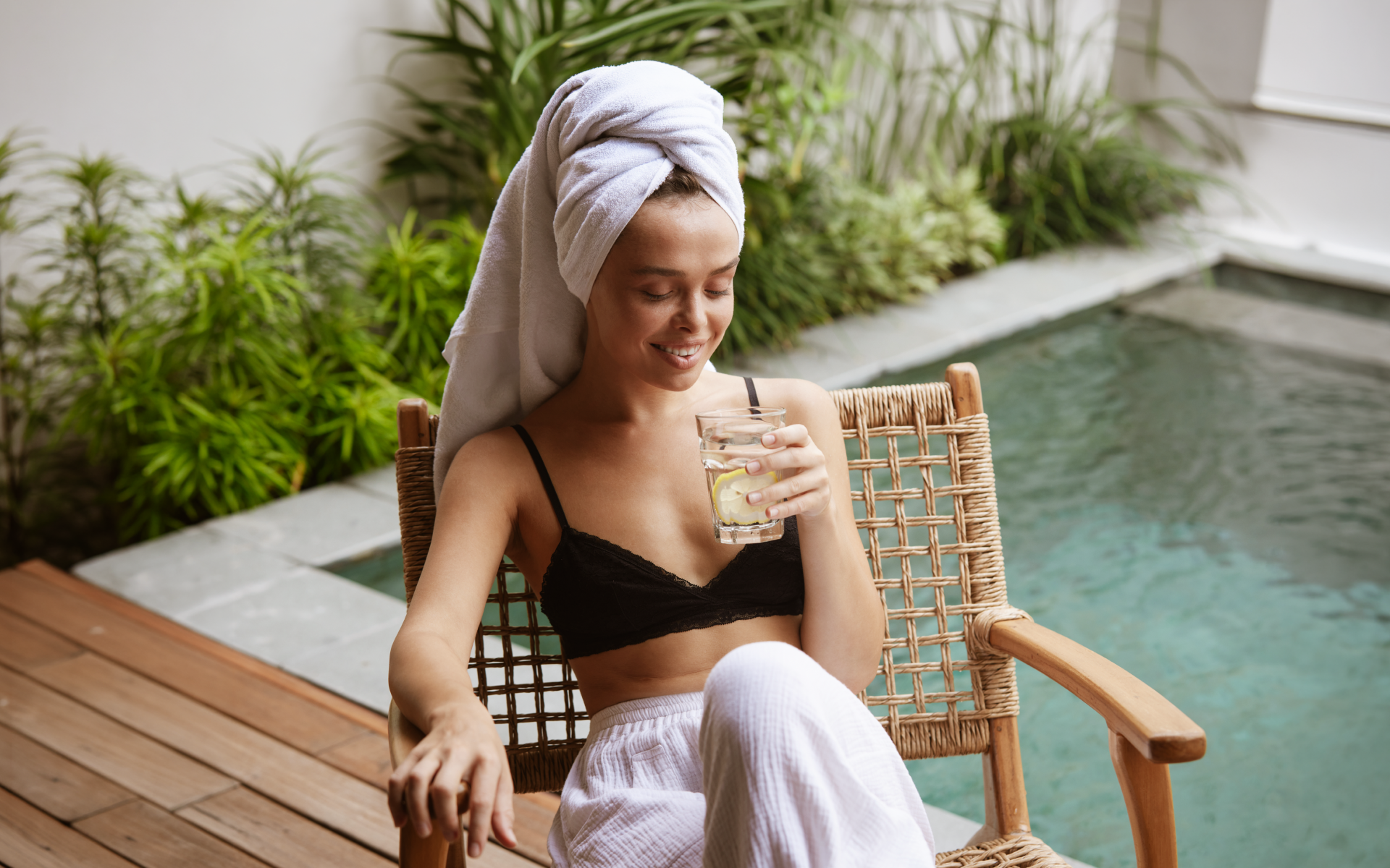 Woman relaxing by a spa pool with a glass of lemon water, illustrating lemon water fasting benefits as part of a calm hydration and wellness routine.