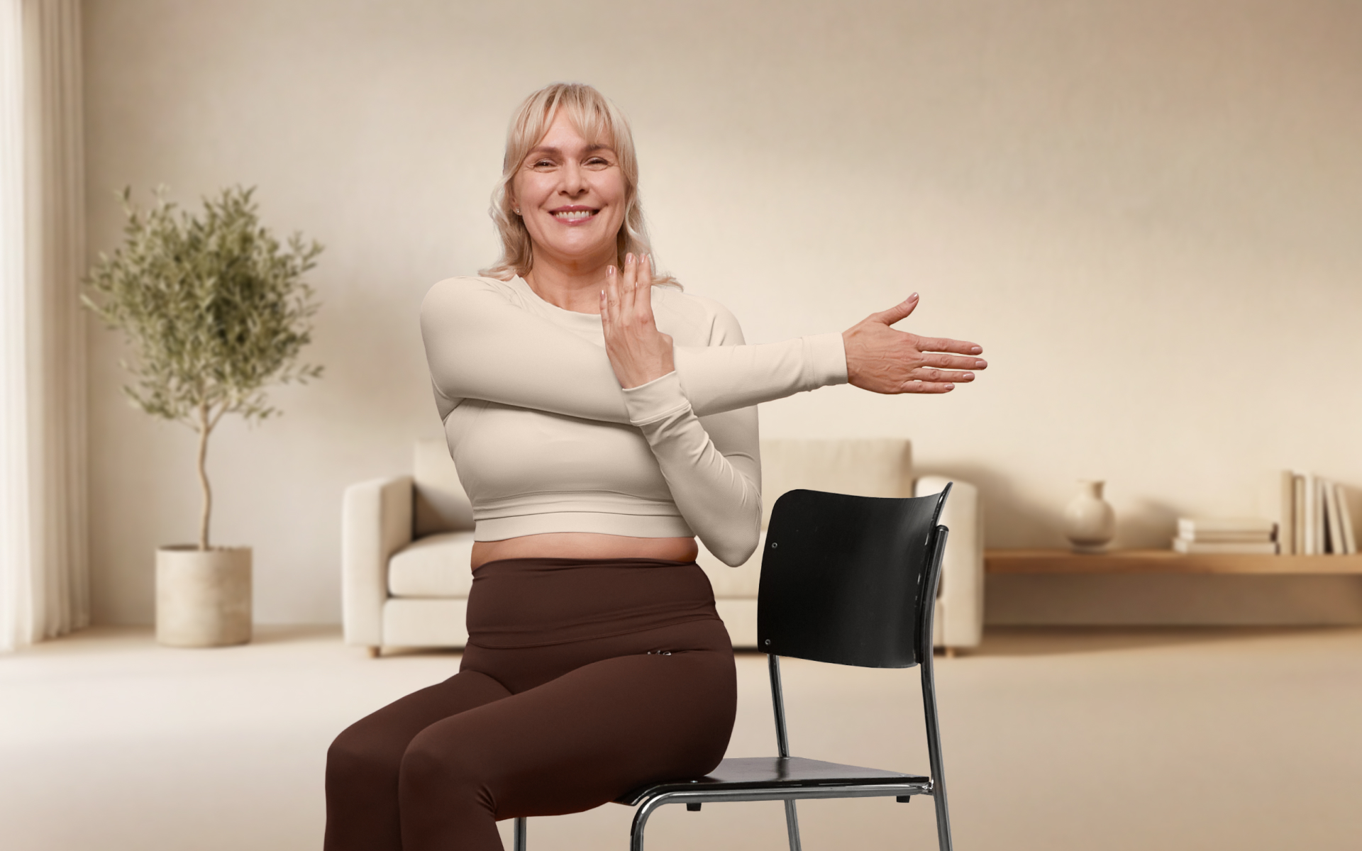 Smiling older woman doing chair based exercises, seated and stretching her shoulder in a calm home setting.