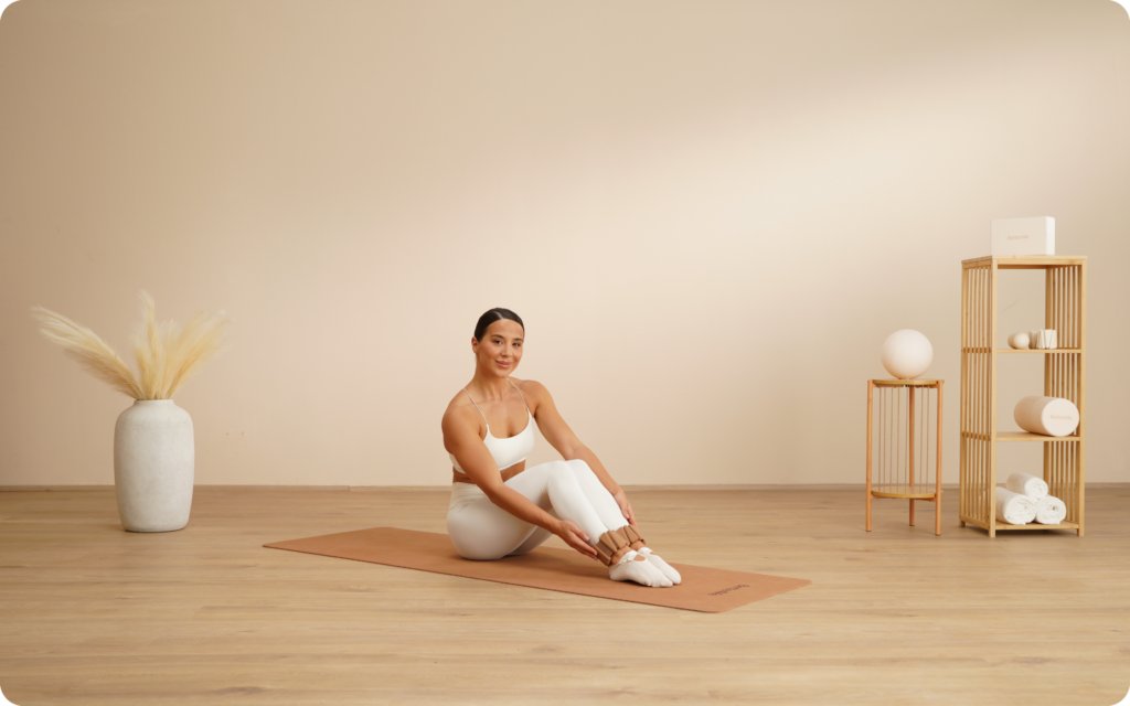 Woman seated on pilates mat fastening ankle weights before a workout