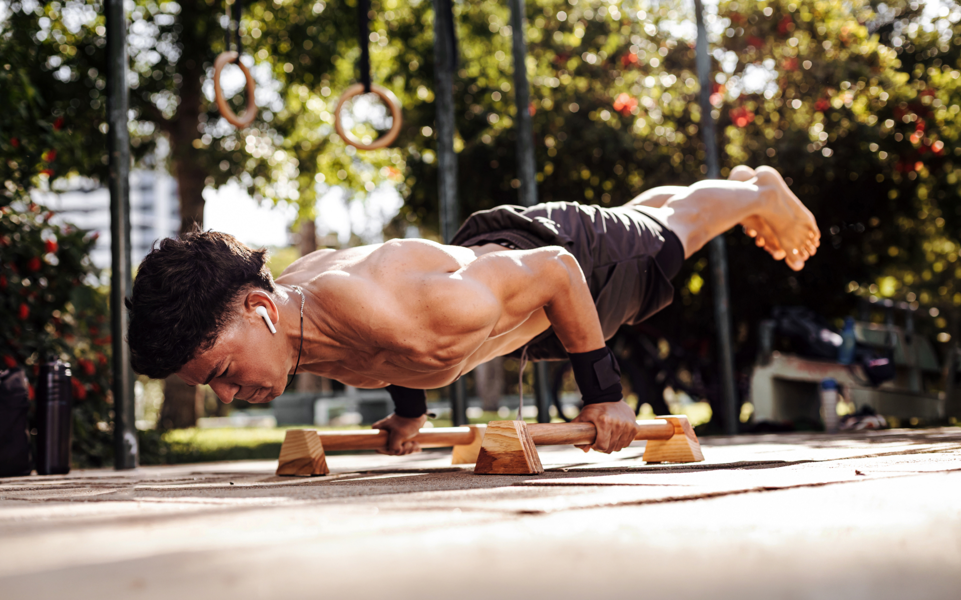 Athletic man performing an advanced bodyweight hold on parallettes outdoors, illustrating a military calisthenics workout for men focused on upper-body strength, balance, and control.