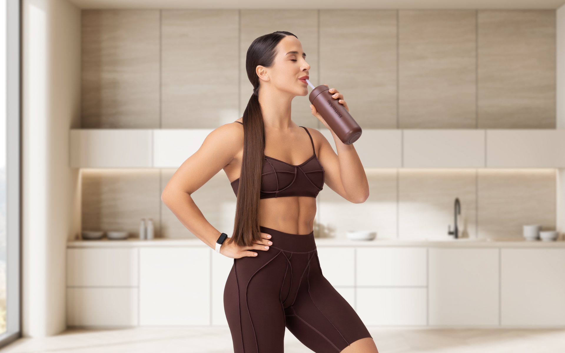 Woman drinking from a bottle in a kitchen, illustrating dry fast vs water fast and hydration during fasting.
