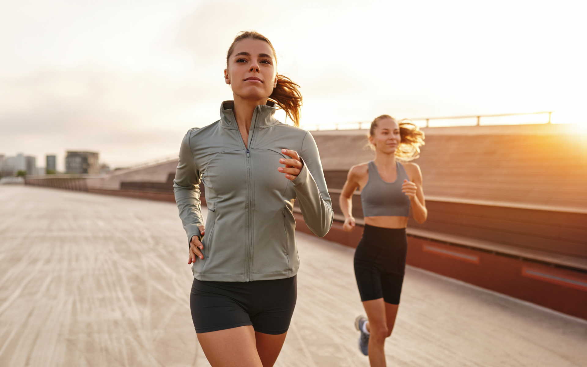 Two women jogging outdoors on a boardwalk at sunrise as part of cross training for runners.