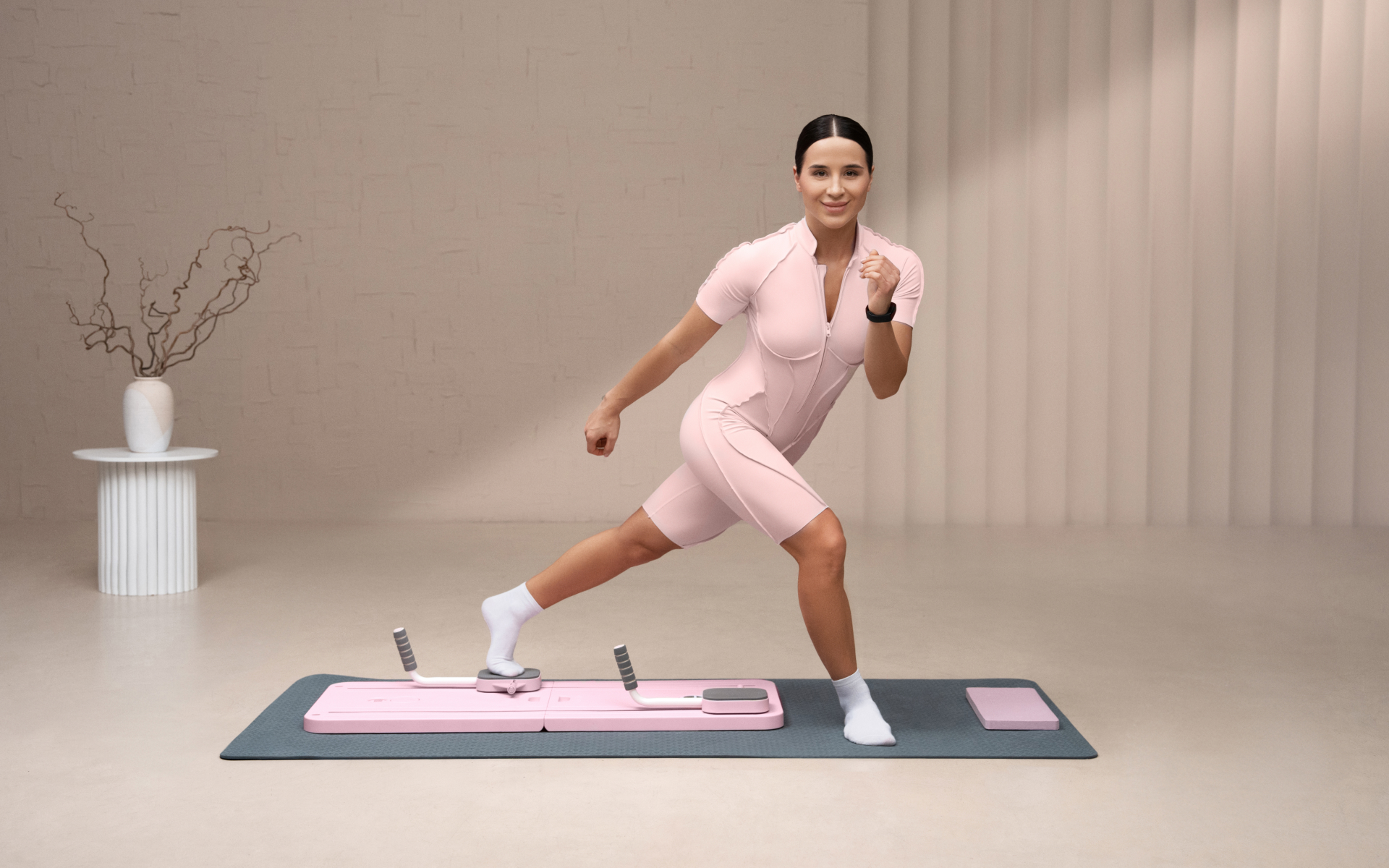 Woman practicing Pilates footwork on a mat with a sliding exercise board in a studio.