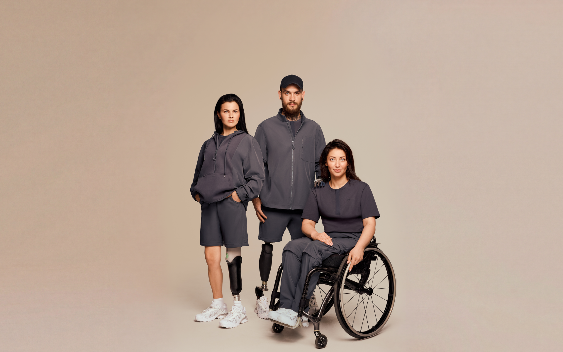 Three models wearing adaptive clothing: navy hoodies, pants, shorts, and a short-sleeve top designed for comfortable, practical, and inclusive everyday style.
