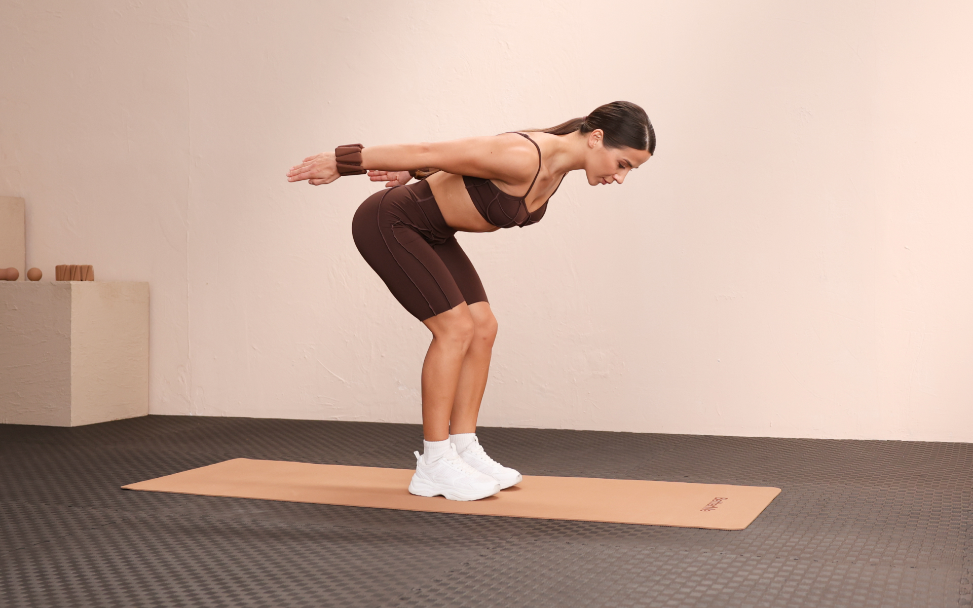 Woman doing bent-over tricep kickbacks with wrist weights on a mat during at home tricep workouts.