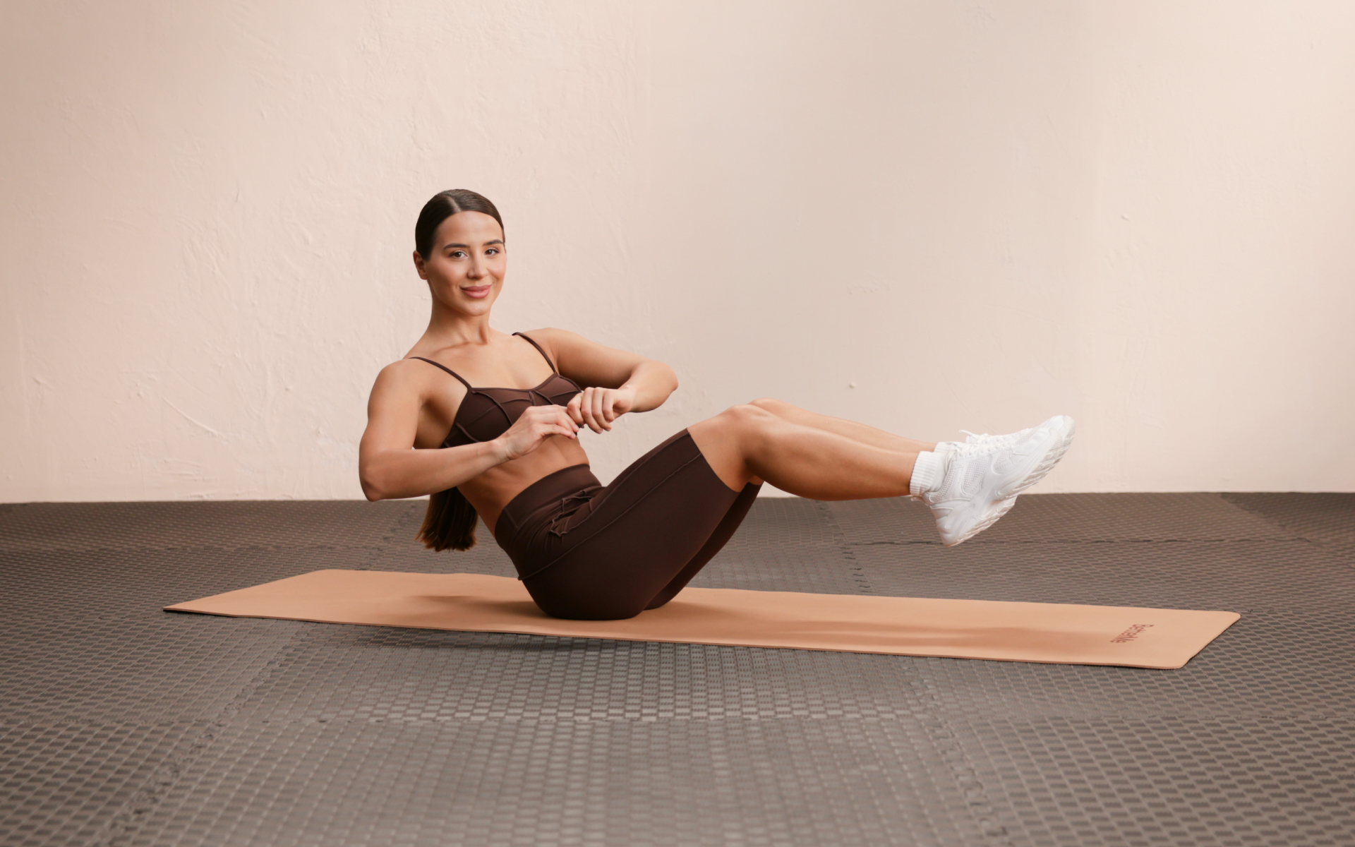Woman holding a boat pose on a mat during a 15 minute calisthenics workout.