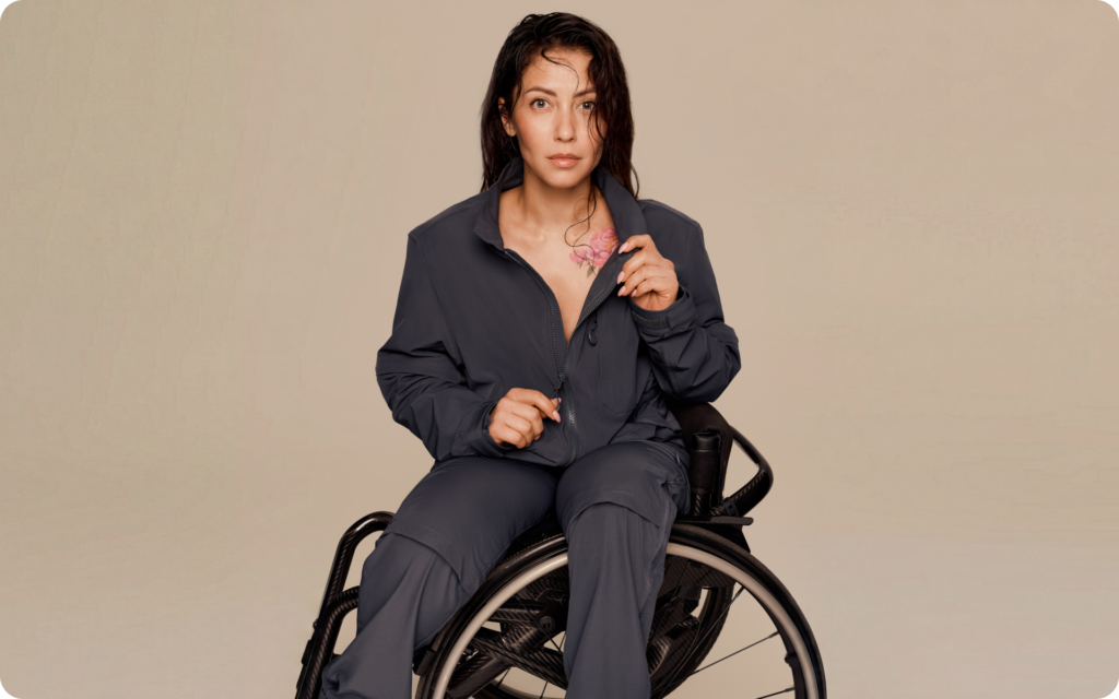 Woman seated in a wheelchair wearing adaptive clothing: a navy zip-front jacket and matching pants designed for comfortable, functional, and stylish everyday wear.