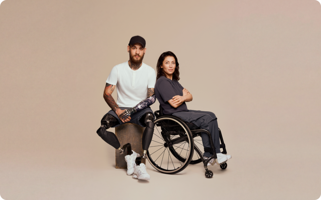 Man with prosthetic limbs and woman seated in a wheelchair wearing adaptive clothing: matching navy lifestyle pieces designed for comfortable, practical everyday wear.