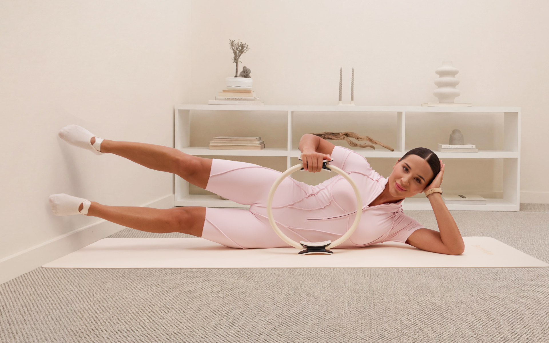 Woman doing side-lying leg lifts with a Pilates ring during at home wall Pilates.