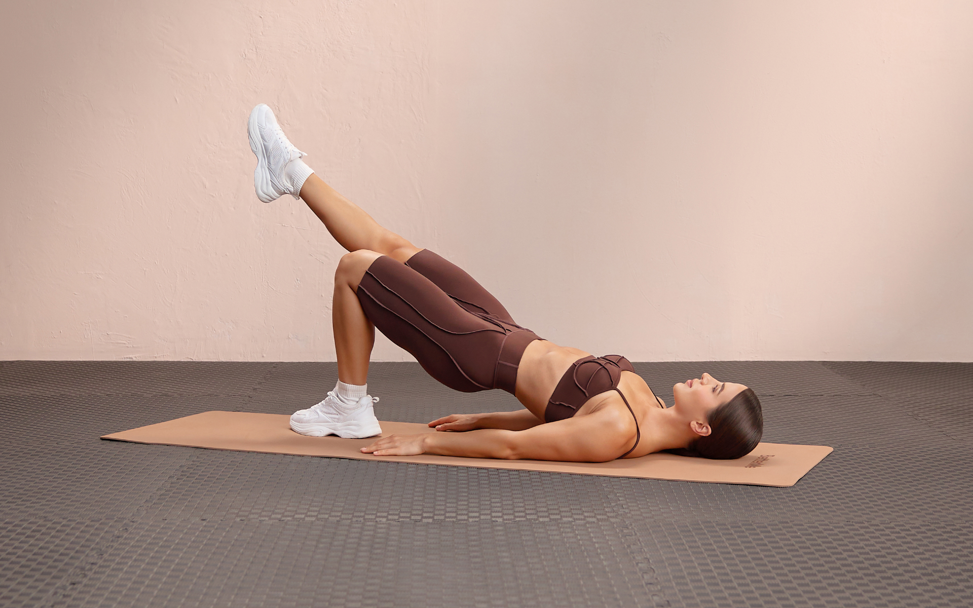 Woman performing a single-leg glute bridge during a calisthenics beginner workout on an exercise mat.