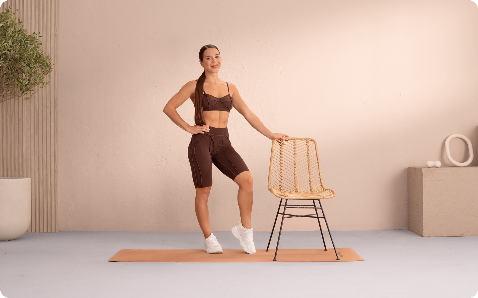 Woman demonstrating diabetes-friendly workouts beside a chair and exercise mat in a bright home fitness space.