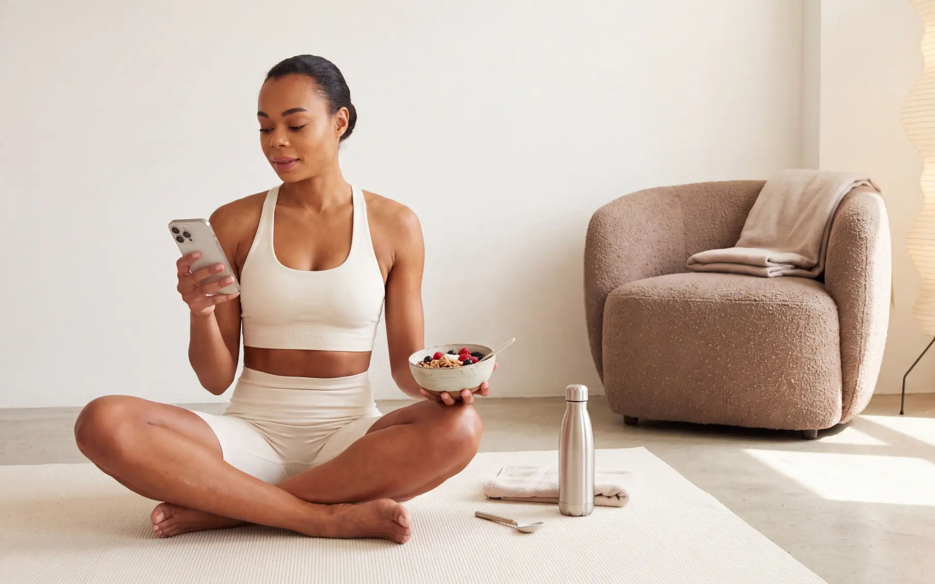 Woman using a fitness app on her phone while holding a bowl of healthy food after a workout.