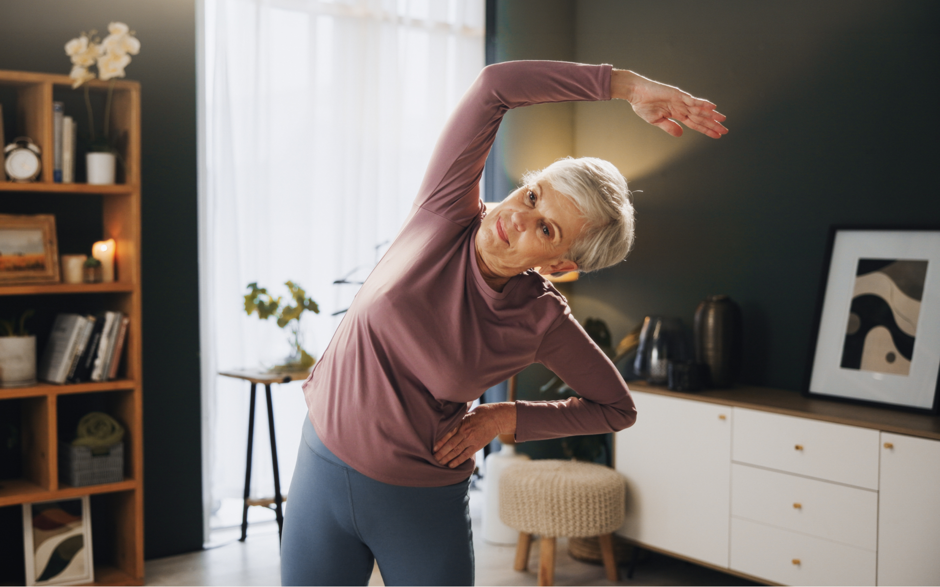 Older woman doing a gentle side stretch at home as part of light exercises.
