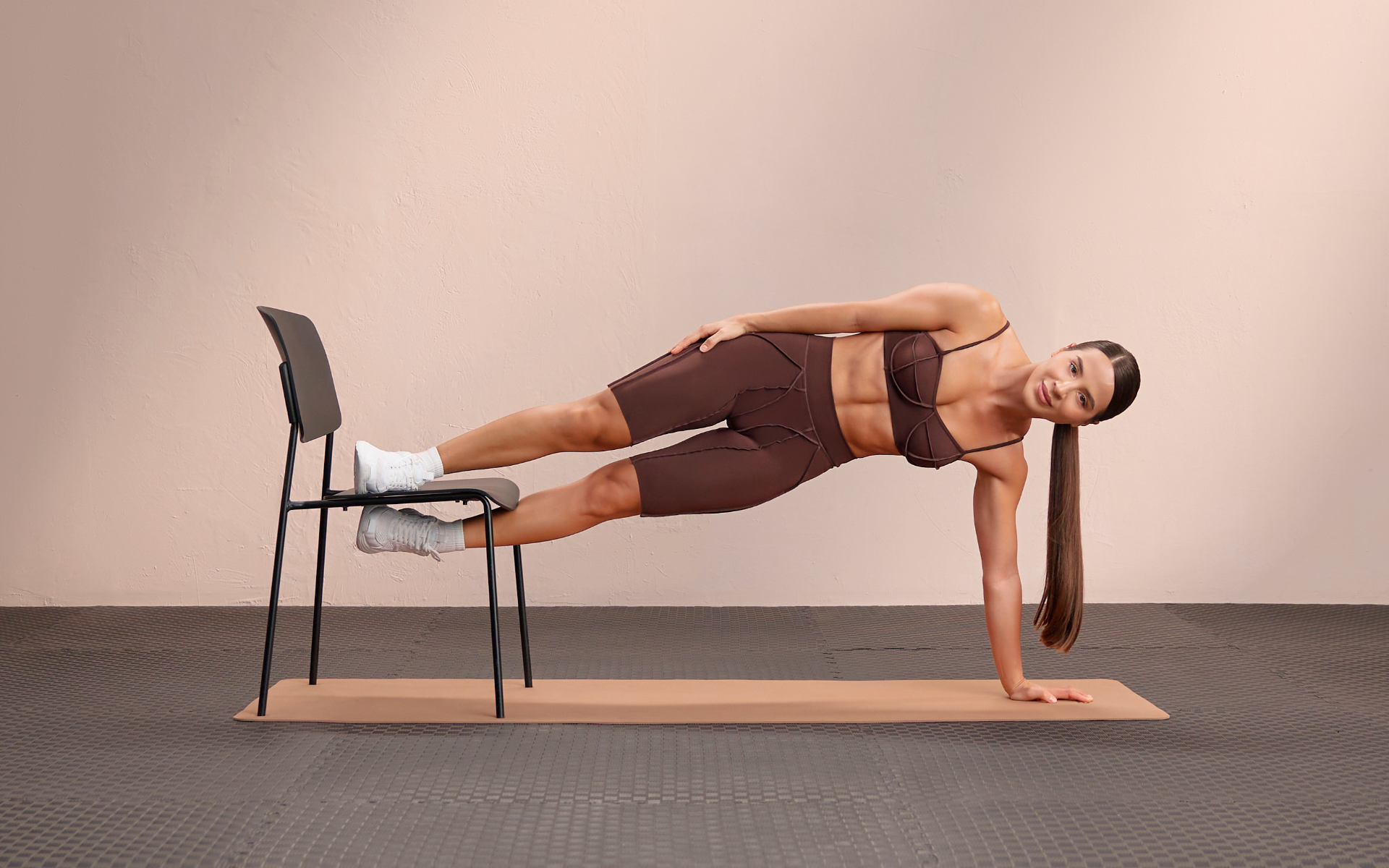 Woman performing an elevated side plank with a chair for a side booty workout.